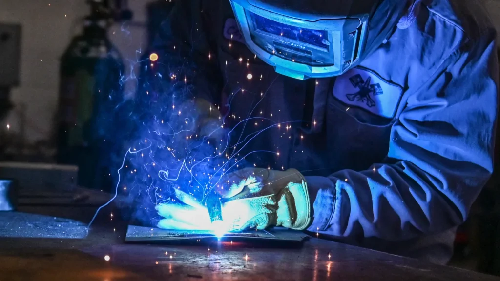 Soldador com máscara trabalhando em peça de metal com faíscas